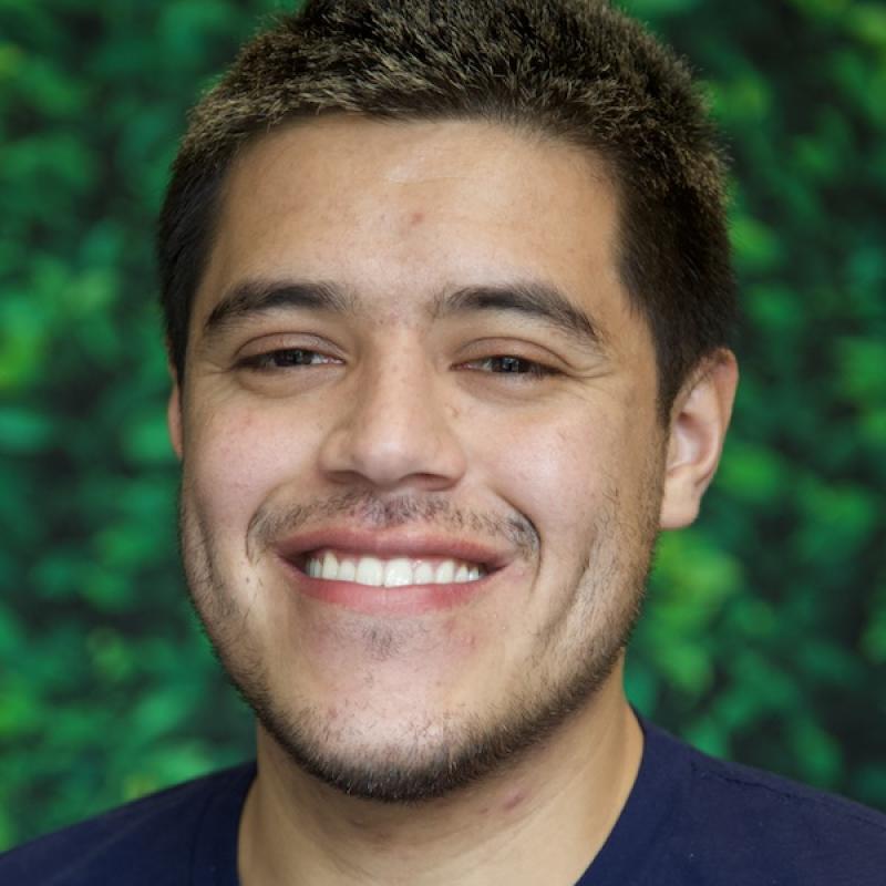 Photo of Isael Andrade with a blue shirt and a green background.